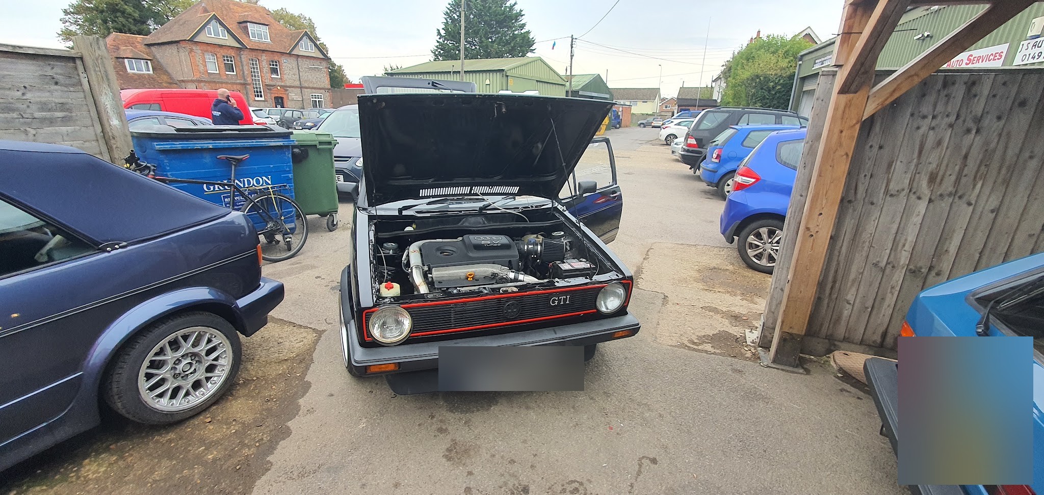 Black Mk1 GTI in the yard with the bonnet up, a blue Mk1 cabriolet alongside